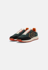 Sneaker verde e nere con motivo a spina di pesce, dettagli bianchi e arancioni, chiusura con lacci e suola in gomma testurizzata.