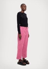 Maglione nero lavorato a maglia con decorazioni sulle spalle, abbinato a pantaloni di velluto a coste rosa larghi e sandali neri con plateau.