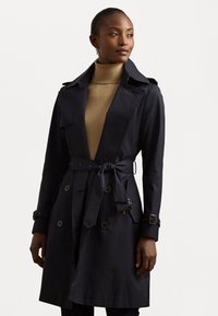 Granatowy trench coat z paskiem w talii, podwójnymi guzikami i kołnierzem. Wykonany z gładkiego materiału o nieco strukturalnym kroju.