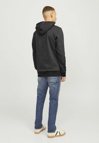 Zwarte hoodie met een zachte textuur, aansluitende manchetten en zoom, gecombineerd met een blauwe spijkerbroek en casual sneakers met crème- en groene accenten.
