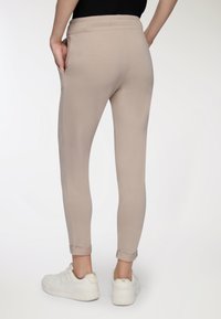 Beżowe dresy o dopasowanym kroju, z elastycznym pasem, bocznymi kieszeniami, mankietami u kostek, noszone z białymi trampkami.