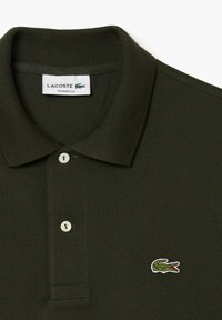 Sötétzöld polóing, texturált anyagból készült, klasszikus gallérral, három gombbal és hímzett Lacoste krokodil logóval.