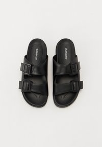 Sorte sandaler med to justerbare spænder, fremstillet af glat materiale. Har en kontureret fodseng og en flad sål.