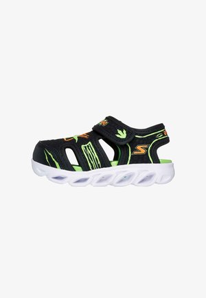 Schwarze und grüne Kindersandalen mit einem atmungsaktiven Design, ausgestattet mit einem Klettverschluss und strukturierten Mustern auf dem Obermaterial. Weiße Sohle.