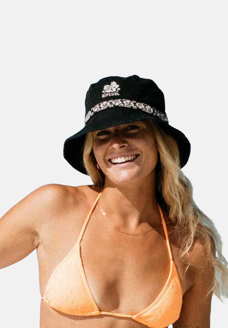Chapeau seau noir avec une bande florale et le logo "Rip Curl", porté avec un haut de bikini orange, sur fond neutre.
