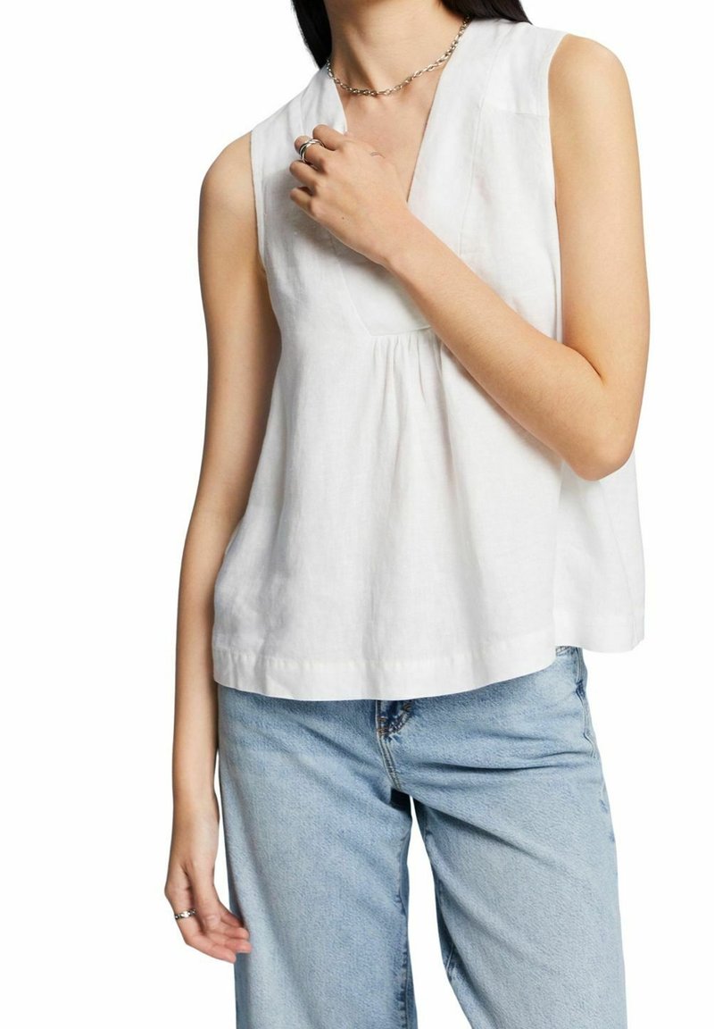 Vit linnetopp utan ärmar med V-ringning och rynkdetaljer, kombinerad med ljusblå denimjeans. Mjuk textur och avslappnad passform.