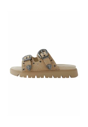 Beige halk sandal med två metallspännen, nitar och en kraftig gummisula med ett räfflat mönster.