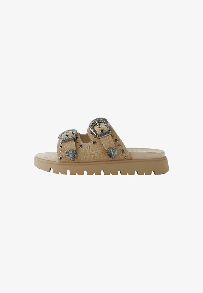 Beige liug sandaalid, millel on kaks metallist nööbiliistuga rihma, stud-detailid ja paks kummine tald, millel on soonikkoes.