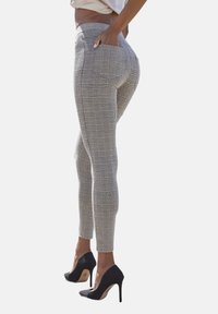 Elastische karierte Hose in Grau und Schwarz, taillierte Passform, mittelhoher Bund, seitliche Taschen, kombiniert mit schwarzen High Heels.