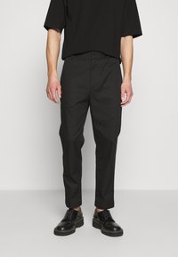Pantalon noir au design droit, taille haute et en coton, associé à des chaussures noires à lacets brillantes.