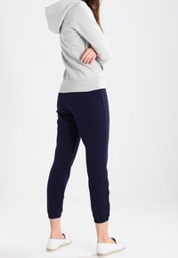 Sweat à capuche en coton gris avec une capuche, associé à un pantalon de survêtement bleu marine fuselé, doté de poignets élastiques, et des chaussures blanches à enfiler avec une semelle tissée.