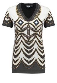 Tričko s krátkým rukávem a véčkovým výstřihem, které má geometrický vzor v černé, bílé a s metalickými zlatými akcenty, doplněné modrými diamantovými detaily.