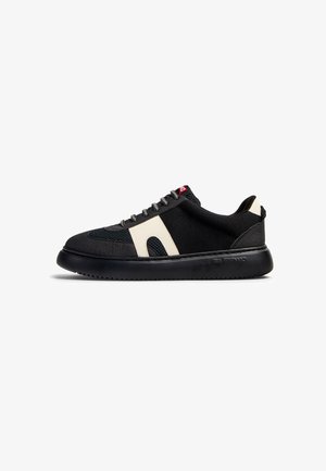 Black sneaker with a textured fabric upper and cream accents. Features a rounded toe, flat black sole, and gray lace closure.