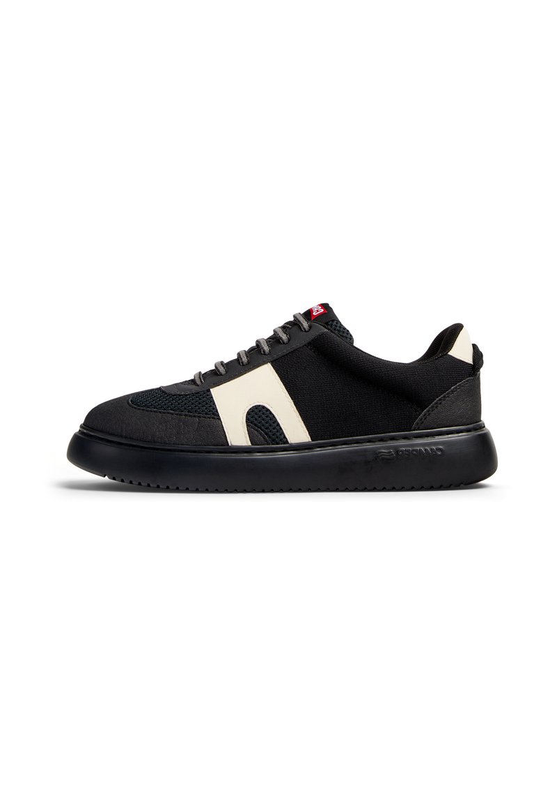 Svart sneaker med ett texturerat tygöverdrag och krämfärgade detaljer. Har en rund tå, platt svart sula och grå snörning.