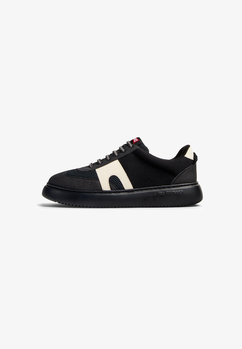 Black sneaker with a textured fabric upper and cream accents. Features a rounded toe, flat black sole, and gray lace closure.