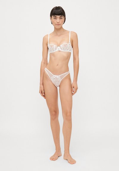 Witte kanten bh en string set met bloemmotieven, verstelbare bandjes en transparant materiaal, met de nadruk op een delicate vormgeving en doorzichtigheid.