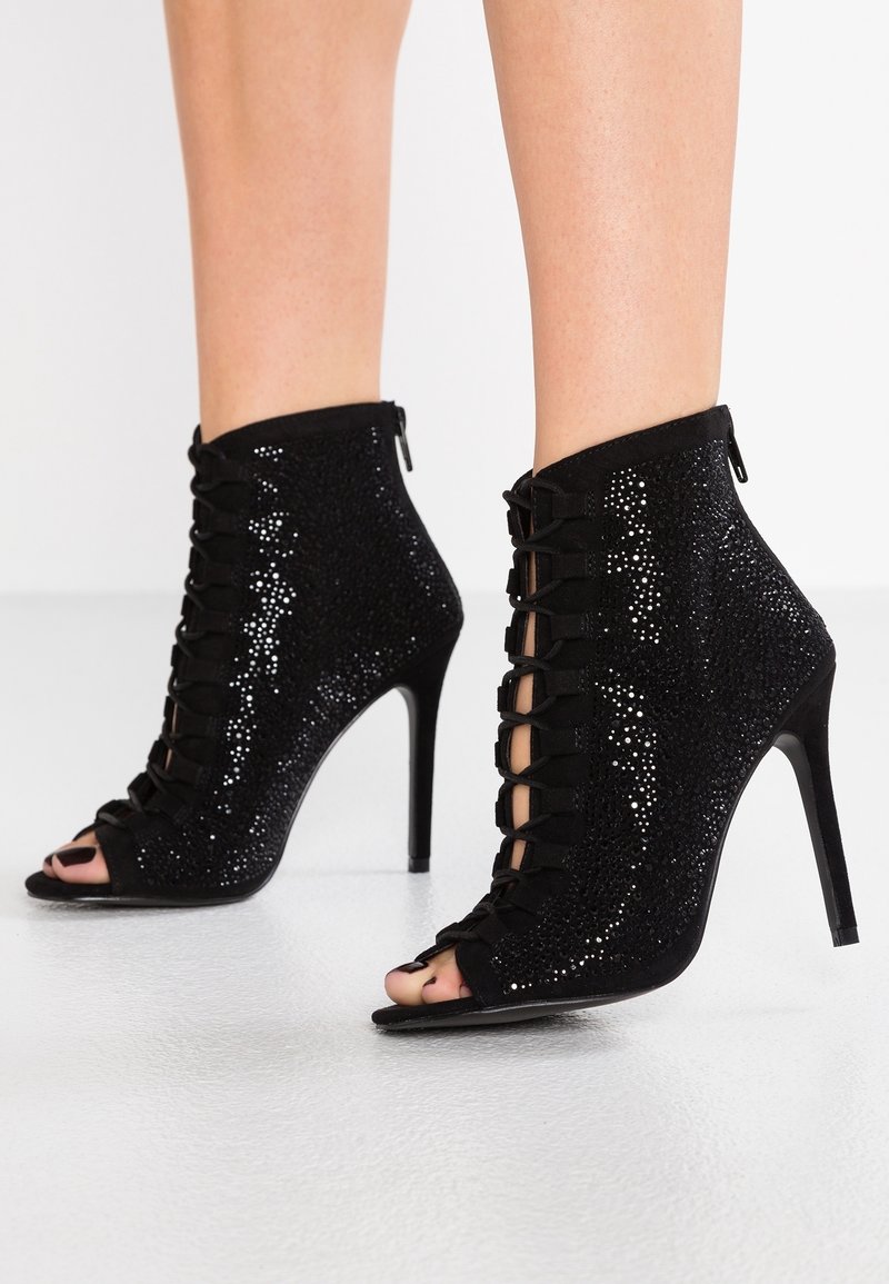 Zwarte enkellaarsjes met open tenen, met een fonkelende textuur, vetersluiting aan de voorkant en hoge stilettohakken. Ritssluiting aan de achterkant.