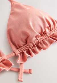 Lyserød bikinitop med bølgende flæsedetaljer, lavet af tekstureret stof. Har justerbare stropper og glitrende accenter over det hele.