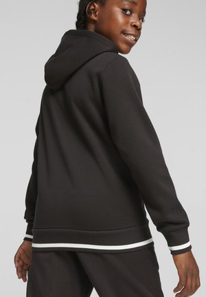 Haut à capuche noir avec un cordon de serrage, des poignets côtelés et un ourlet inférieur présentant des rayures blanches. Tissu doux avec une coupe décontractée.