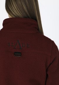 Bordowa polarowa kurtka o miękkiej fakturze, z wysokim kołnierzem i czarnym haftowanym logo "SLADE" na plecach. Zawiera czarny akcent w postaci elementów metalowych.