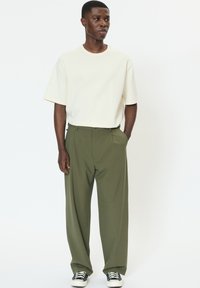 Világosbézs, túlméretezett póló, magas derekú, bőszárú olívazöld nadrággal és fekete-fehér tornacipővel párosítva. Egyszerű dizájn, minták nélkül.