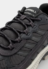 Dunkelgrauer Sportschuh aus einem Mix aus Mesh- und Synthetikmaterial, mit strukturierten Akzenten, flachen Schnürsenkeln und einer weißen Gummisohle.