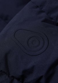 Chaqueta aislante azul marino con una textura suave y un distintivo logo circular emblema en la tela.