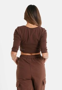 Brun cropped langærmet top med rund halsudskæring og tætsiddende ærmer, lavet af blødt stof, båret med matchende brune bukser.
