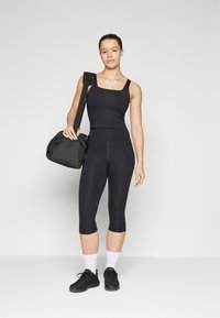 Czarny sportowy top bez rękawów i skrócone legginsy, w połączeniu z czarnymi sneakersami i białymi skarpetkami. Trzyma czarną torbę sportową. Prosty design.