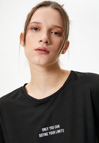 Camiseta deportiva negra con cuello redondo y una tela texturizada. En la parte delantera tiene un texto en blanco: "SOLO TÚ PUEDES DEFINIR TUS LÍMITES."