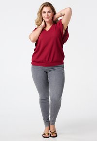 Haut texturé bourgogne avec un col en V et des manches courtes, associé à un jean skinny gris et des sandales noires avec des accents dorés.
