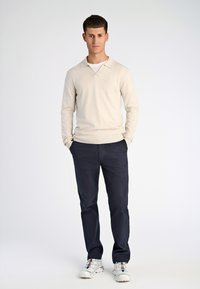 Ljusbeige långärmad pikétröja med krage, kombinerad med marinblå chinos och vita sneakers med färgade detaljer. Enkel design, inga mönster.