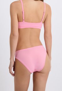 Set di bikini rosa con bralette a chiusura posteriore e slip a vita alta. Texture liscia e design minimal con spalline regolabili.