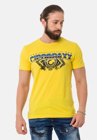 Yellow cotton t-shirt featuring a graphic print with blue and black accents. Short sleeves and round neckline. Casual fit with a smooth texture.