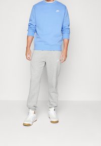 Sudadera azul clara con puños y cuello acanalados, combinada con pantalones de chándal grises que tienen una cintura elástica y un pequeño logo. Zapatillas blancas con suela de goma.
