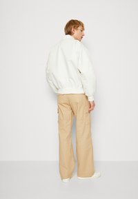 Chaqueta bomber blanca con puños y dobladillo de canalé, combinada con pantalones cargo beige con bolsillos laterales. Textura de tela suave, ajuste relajado.