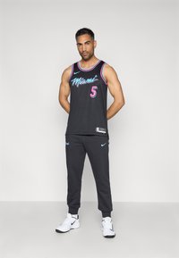 Μαύρο αμάνικο τζέρσεϊ με την ένδειξη "Miami" και τον αριθμό "5" σε ροζ και μπλε, συνδυασμένο με μαύρους τζόγκερ, με τον λογότυπο της Nike και λευκά παπούτσια.