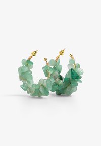 Pendientes de aro con piedras preciosas verdes de formas irregulares, con herrajes de oro y un acento de alambre enrollado. Presentan una apariencia natural y texturizada.