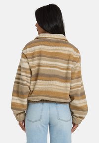 Giacca corta e fuzzy in beige con strisce marroni e grigie. Dotata di colletto e maniche ampie, realizzata in materiale morbido e testurizzato.