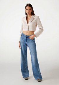 Kropsnær beige blazer med hakrevers og 3/4-lange ærmer, kombineret med lyseblå jeans med vide ben, frontlommer og en falmet vask.