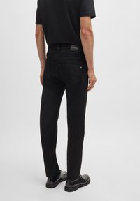 Black denim jeans with a slim fit, featuring rear pockets and a branded leather patch. Worn with black shoes and a black top.