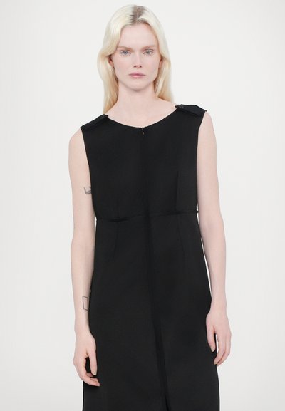 Robe sans manches noire avec fermeture éclair sur le devant, poches latérales et accents de bouton sur les épaules. Tissu doux, silhouette épurée.