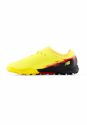 Yellow and black turf soccer shoe with red accents and textured upper, without laces, showing New Balance logo on heel side.