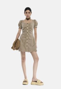 Tan kordfløjlskjole med puffærmer, for-trykknapper og sidelommer. Båret med chunky beige platformsandaler og en strik-taske.