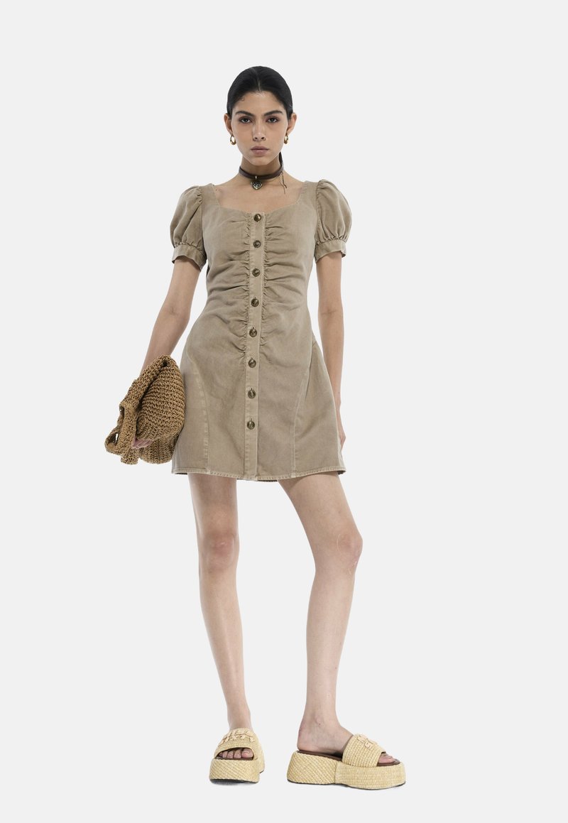 Tan kordfløjlskjole med puffærmer, for-trykknapper og sidelommer. Båret med chunky beige platformsandaler og en strik-taske.