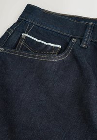 Tmavě modré džínové kalhoty s kontrastním žlutým prošitím, pěti kapsami a tradičním pasem. Slim fit, s malou mincovní kapsou.