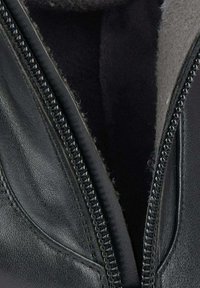 Close-up van een gedeeltelijk open ritssluiting van een zwarte leren jas, met gedetailleerde stiksels en een zachte binnenvoering.