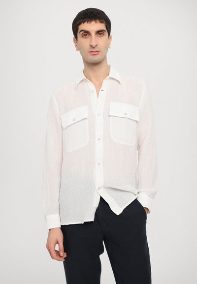 White, long-sleeve shirt made of lightweight fabric with two front pockets and button closure. Paired with navy trousers.