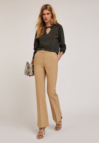 Haut à manches longues noir pailleté avec décolleté en trou de serrure, associé à un pantalon beige sur mesure, et accessoirisé avec un sac à main en simili-cuir à texture serpent.