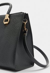 Sort struktureret håndtaske med tekstur, flet-åndtag og guldfarvede detaljer. Har en aftagelig skulderrem.